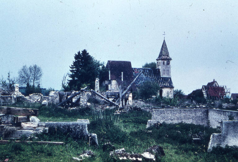 Historische Fotografie des verlassenen Münsingen-Gruorn. Es sind noch Mauer- und Gebälkreste zu sehen sowie im Hintergrund die Kirche von Gruorn.