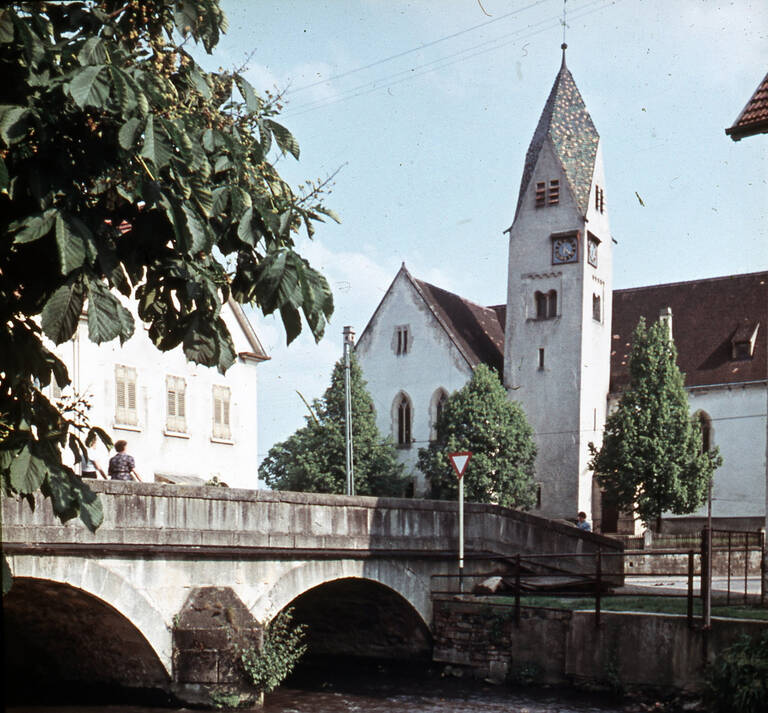 Historische Fotografie der Mauritiuskirche Reutlingen West-Betzingen. Im Vordergrund ist eine Brücke über die Echaz zu sehen.