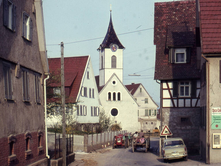 Historische Fotografie einer Straße in Reutlingen-Sickenhausen. Im Hintergrund ist eine Kirche zu sehen.